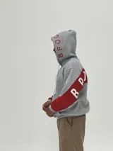 Canguro gris con capucha, de corte holgado, con detalles en color rojo en las mangas y estampado de texto en color rojo en la capucha y el pecho.