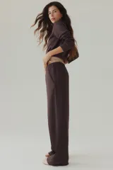 Pantalón de corte holgado en punto pesado con leve brillo, color marrón, con elástico revestido en la cintura, bolsillos al bies y piernas rectas con pliegues cosidos.
