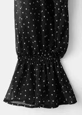 Vestido midi de gasa negro con estampado de lunares blancos, cuello alto, manga larga con volados en los puños y falda con vuelo.