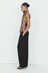 Pantalón negro de tiro alto, corte amplio estilo balloon o culotte, con pliegues marcados en el delantero y bolsillos laterales ocultos.