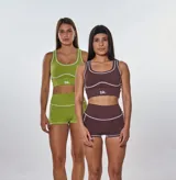 Conjunto deportivo de dos piezas color marrón, compuesto por un top deportivo con cuello redondo y costuras decorativas en contraste, y un short de tiro alto con costuras laterales a juego. El top presenta el logo 'bk.' estampado en el frente.