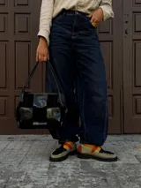 Cartera de mano tipo shopper con diseño de damero, combinando paneles de cuero liso y gamuza en color negro. Cuenta con asas trenzadas y cierre superior.