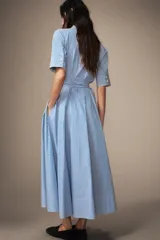 Vestido midi de algodón con estampado de rayas verticales, cuello solapa, manga corta con puños y cierre frontal de botones. Presenta bolsillos con solapa en el pecho y un cinturón de la misma tela para ajustar la cintura.