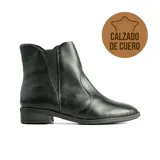 Bota baja tipo chelsea de cuero negro con textura granulada, elásticos laterales y suela plana con pequeño taco cuadrado.