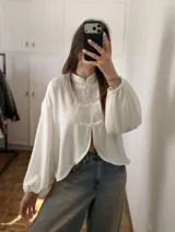 Blusa blanca con cuello mao, mangas globo con puños elásticos y cierre frontal con alamares.
