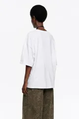 Camiseta negra de corte recto y largo medio, confeccionada en algodón orgánico. Presenta escote redondo, mangas cortas amplias con costuras raglán y detalles de cortes diagonales en el cuerpo.