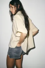 Shorts de jean de algodón, tiro alto, color azul claro desgastado. Presenta cinco bolsillos, cierre frontal con botón metálico y cremallera, y bajo desflecado con vuelta.