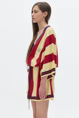 Bata tipo kimono a la rodilla, con rayas verticales rojas y amarillas y cuello en V azul marino. Tiene un logo bordado en el pecho y un lazo en la cintura.