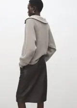 Jersey de punto color beige, con cuello polo, escote en V y mangas largas con puños ajustados. Presenta una textura acanalada y un diseño holgado.