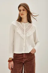 Camisa de manga larga color negro, con cuello redondo y cierre frontal de botones. Presenta un diseño con volados en la parte superior delantera y detalles de encaje bordado en los hombros y pecho.