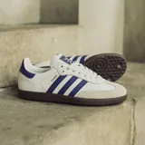 Championes Adidas Samba ADV, color blanco con detalles en violeta y suela marrón.