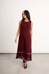 Vestido largo de punto color bordó con diseño sin mangas, cuello redondo y detalles de ribete en color celeste en el cuello, sisas, ruedo y a lo largo de la parte inferior, culminando en un acabado calado con volados.
