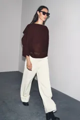 Jersey de punto color vino tinto, de corte amplio y holgado, con cuello bote y un detalle de capa asimétrica superpuesta en la parte superior delantera. Mangas anchas tipo murciélago.