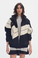 Campera oversize de denim en color negro y crudo, con diseño geométrico en bloques, cuello alto, cierre frontal y bolsillos.