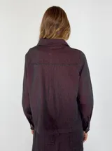 Chaqueta tipo camisa de denim color borgoña, con cuello clásico, manga larga, cierre frontal con botones y bolsillo de parche en el pecho.