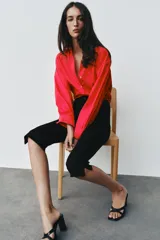 Camisa de popelina roja, de corte oversize, con cuello solapa, manga larga y bajo asimétrico redondeado. Cierre frontal oculto con botones.