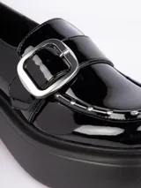 Zapatos tipo mocasines negros con plataforma de 6cm, hebilla metálica plateada y pequeños detalles plateados en la capellada.