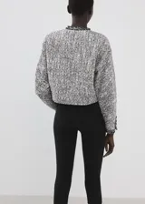 Chaqueta de tweed en tonos gris y blanco, con cuello redondo, manga larga, bolsillos frontales de ribete y cierre delantero con botones.