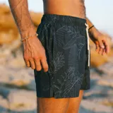 Short de baño negro con estampado botánico de hojas en líneas finas blancas. Cuenta con cintura elástica con cordón ajustable, dos bolsillos laterales y uno trasero.