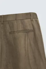 Pantalón de corte relajado confeccionado en mezcla de algodón y lino, con diseño de pliegues frontales, bolsillos laterales y bolsillos traseros de vivo. Presenta cierre frontal con cremallera y botón, con un acabado de lavado especial que le otorga una apariencia única.