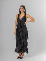 Vestido largo negro de seda con escote en V adornado con lentejuelas plateadas. Presenta un diseño de capas superpuestas con terminaciones deshilachadas que aportan volumen y movimiento. Es de corte sin mangas con breteles anchos y espalda elastizada.