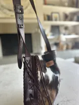 Bolso maxi de cuero con estampado de vaca en blanco y negro, y cuero color chocolate en la parte posterior. Tiene correa larga para colgar al hombro.