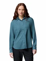 Camisa de senderismo Columbia de manga larga en color azul petróleo, confeccionada en tejido técnico con tecnología Omni-Wick y Omni-Shade. Presenta cuello clásico, cierre frontal con botones, dos bolsillos frontales con solapa y ventilaciones traseras de malla para mayor transpirabilidad.