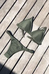 Bikini de dos piezas color marrón, con corpiño triangular fijo con corte bajo el busto, breteles regulables con hebilla y almohadillas desmontables. La bombacha es vedetina con frunce elástico en los costados.