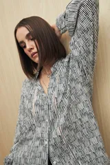 Camisa de calce relajado con estampado lineal irregular en blanco y negro. Presenta cuello clásico, abotonadura frontal, mangas largas con puños camiseros y detalles de recortes verticales en el frente.