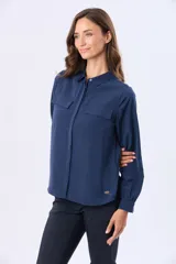 Blusa tipo camisa de manga larga en color azul marino, confeccionada en tela suave y sedosa con doble capa en el frente. Presenta cuello clásico, cierre frontal con botones ocultos y un bolsillo en el pecho.