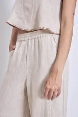 Pantalón de lino color beige, de corte amplio y tiro alto, con cintura elástica y bolsillos laterales.