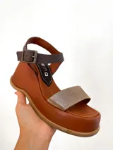 Sandalias de cuero color marrón con plataforma y tira delantera dorada. Tira trasera marrón con hebilla metálica.