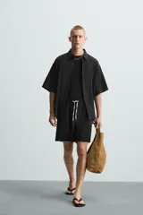 Bermuda negra de corte regular, confeccionada en tejido jacquard con efecto arrugado. Presenta cintura elástica ajustable con cordón blanco, bolsillos laterales y bolsillos traseros de vivo.