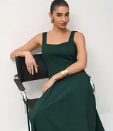Vestido midi de corte evasé, color verde oscuro, con escote cuadrado, breteles anchos y recortes verticales que definen la silueta.