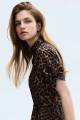 Vestido midi con estampado de leopardo, cuello camisero, botones frontales y mangas cortas con detalle de lazos. Cuenta con una costura fruncida con cinturón para atar en la cintura y falda con leve vuelo.
