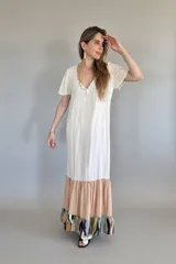 Vestido largo de manga corta con cuello en V, de color crema liso en la parte superior. La falda es de corte amplio con un volante en color melocotón liso, y un volante inferior con estampado abstracto en tonos verde oliva, negro, naranja y azul claro.