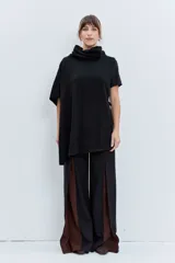 Poncho de punto asimétrico color negro, con cuello alto tipo polera y diseño de manga corta en un lado, ofreciendo una caída fluida y holgada.