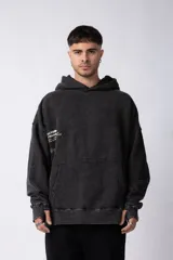 Buzo canguro con capucha, de calce oversize y efecto de lavado gastado en color negro. Presenta un bolsillo frontal tipo canguro y un estampado gráfico pequeño en el lado derecho del pecho.