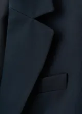 Chaqueta entallada azul marino con cuello de solapa con muesca, hombros estructurados, cierre frontal de un botón, bolsillos de ribete en la parte delantera y manga larga con puños abotonados.