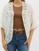 Cardigan abierto estilo kimono, color crudo, con mangas amplias al codo. Presenta una base con textura y motivos florales bordados a tono, con paneles de encaje calado estilo macramé en el frente, puños y ruedo.