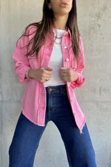 Sobrecamisa rosa de denim con terminaciones desflecadas, cuello camisero, cierre frontal con botones metálicos, dos bolsillos de parche en el pecho y mangas largas con puños abotonados.