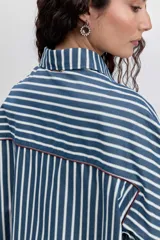 Camisa de manga larga a rayas verticales azul marino y blancas, con cuello clásico, bolsillo de parche en el pecho y ribetes finos en color rojo.