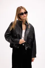 Campera corta de cuero sintético en color beige, con diseño de calce relajado, cierre frontal metálico, bolsillos con solapa en el frente y cordón ajustable en el ruedo.