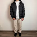 Campera inflada negra con capucha, cierre frontal blanco y puños elásticos acanalados. Presenta el logo de la marca Santa Barbara Outfitters bordado en el pecho.