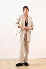 Blazer de cuero sintético color beige, con diseño de doble botonadura, solapas clásicas y bolsillos frontales con solapa.