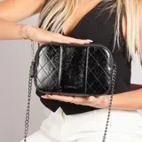 Cartera bandolera negra con diseño matelaseado y correa de cadena metálica.