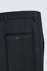 Pantalón de traje negro de corte regular fit, con pinzas delanteras, bolsillos laterales y cierre frontal con cremallera y botón.