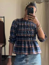 Camisa de manga tres cuartos con diseño a cuadros en tonos azul y naranja. Presenta un cuerpo con frunces elásticos que crean un efecto ajustado y volados en el cuello y los puños.