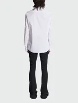 Camisa blanca de popelina de algodón con cuello clásico, cierre frontal con botones ocultos, mangas largas con puños abotonados y bordado con el logo de la marca en cuello y puños.