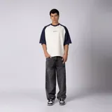 Remera de jersey de algodón con diseño bicolor, cuerpo en color crudo y mangas raglán en azul marino. Presenta escote redondo de ribb y un pequeño estampado gráfico en el centro del pecho.